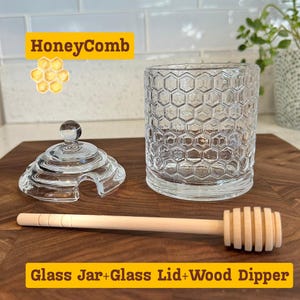May include: A clear glass honey jar with a honeycomb pattern, a glass lid, and a wooden honey dipper. The jar and lid are made of clear glass. The wooden dipper is light brown. The text "HoneyComb" and "Glass Jar+Glass Lid+Wood Dipper" are in the image.