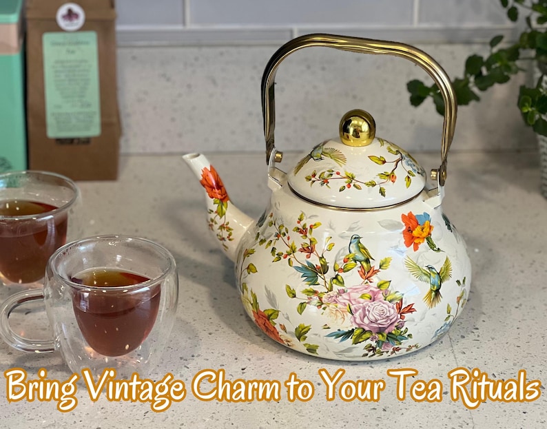 Pu&ograve; includere: Una teiera in smalto bianco con manico e pomello dorati, ornata da motivi floreali e di uccelli. Due tazze di t&egrave; in vetro trasparente sono davanti alla teiera. Il testo "Bring Vintage Charm to Your Tea Rituals" &egrave; in basso.