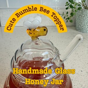 May include: A handmade glass honey jar with a bumble bee topper. The jar is filled with honey and includes a glass spoon. The bumble bee topper is yellow and white. The text "Cute Bumble Bee Topper" and "Handmade Glass Honey Jar" are in the image.