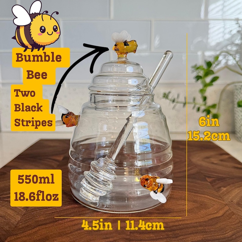 May include: A clear glass honey jar with a bee-shaped lid and two bee-shaped embellishments. The jar includes a glass honey dipper and holds 550ml or 18.6 fl oz. It measures 4.5 inches wide and 6 inches tall.