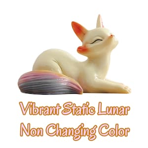 Puede incluir: Una figura de zorro de color crema en posici&oacute;n de descanso con los ojos cerrados. El zorro tiene las puntas de las orejas naranjas y una gran cola multicolor con tonos violeta, rosa y azul. Debajo del zorro est&aacute; el texto: Vibrant Static Lunar Non Changing Color.