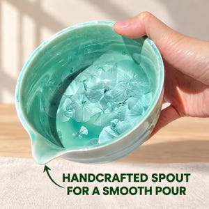 May include: A ceramic pouring bowl featuring a glossy, light turquoise glaze with crystalline patterns throughout the interior. The bowl includes a small, integrated pouring spout and text at the bottom that reads: HANDCRAFTED SPOUT FOR A SMOOTH POUR.