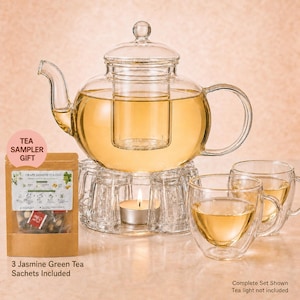 May include: A clear glass teapot with a removable infuser sits on a glass warmer base containing a lit tea light candle. Two double-walled glass cups filled with tea are nearby. A brown paper pouch labeled Grape Jasmine Oolong is included.