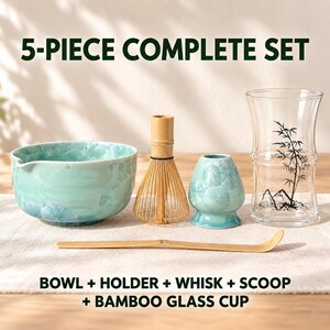 May include: A 5-piece matcha set including a light blue ceramic bowl, a bamboo whisk, a matching ceramic whisk holder, a bamboo scoop, and a clear glass cup with a black bamboo and mountain graphic. Text reads 5-PIECE COMPLETE SET and BOWL + HOLDER + WHISK + SCOOP + BAMBOO GLASS CUP.