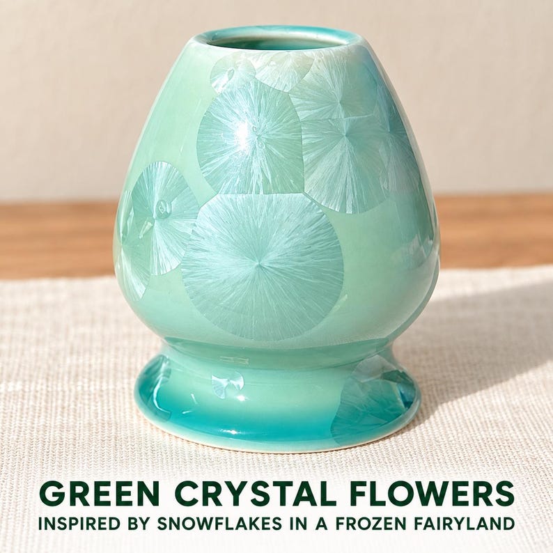 May include: A bulbous ceramic vase featuring a glossy mint green glaze with white crystalline flower patterns. The base is a darker teal hue. The text GREEN CRYSTAL FLOWERS INSPIRED BY SNOWFLAKES IN A FROZEN FAIRYLAND is printed below the object.