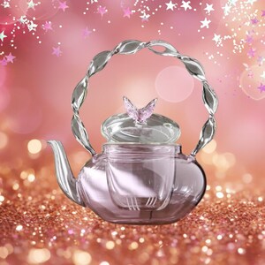 May include: A clear glass teapot with a silver handle and a butterfly-shaped lid. The teapot has a built-in infuser and sits on a glittery surface. The background is a soft pink with star-shaped confetti.