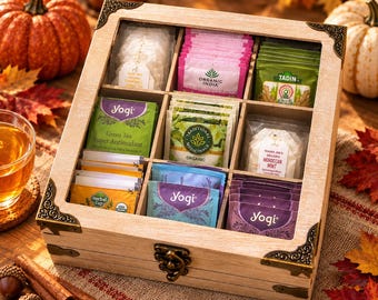 May include: A square wooden tea storage box with a clear lid and nine internal compartments. The box features decorative metal corner accents and a front latch. Inside are various tea bags from brands including Yogi, Organic India, and Tadin.