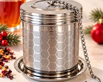 May include: A cylindrical stainless steel tea infuser featuring a honeycomb mesh pattern and the text SUS304 engraved on the side. The infuser includes a removable lid, a matching circular drip tray, and a metal chain with a hook at the end.