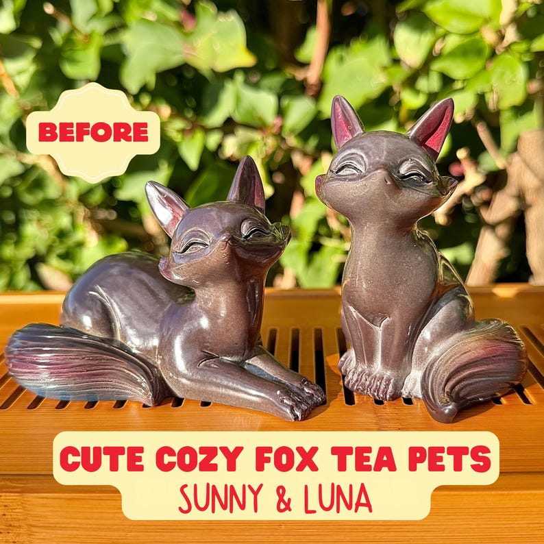 Puede incluir: Dos figuras de zorro de color morado oscuro con superficies lisas y brillantes. Un zorro est&aacute; tumbado con la cola enroscada, mientras que el otro est&aacute; sentado. El texto BEFORE, CUTE COZY FOX TEA PETS y SUNNY & LUNA es visible en rojo y amarillo.