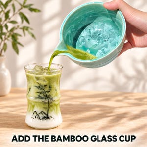 May include: A clear glass cup shaped like a bamboo stalk with a black ink illustration of bamboo and mountains, filled with a layered green matcha latte and ice, being poured into from a light blue ceramic bowl with a crystalline interior.
