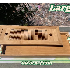 May include: A large, rectangular bamboo tea tray with a removable top featuring a slatted design and a circular hole. The tray measures 38.5 inches long, 6 inches wide, and 1.2 inches deep. The word "Large" is printed on the top right.