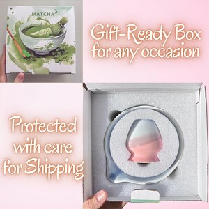 May include: A white cardboard box featuring a green matcha tea illustration and the text MATCHA. Inside, a white foam insert holds a small, two-toned ceramic whisk holder that transitions from white at the top to a soft pink at the base.