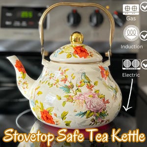 Pu&ograve; includere: Teiera da piano cottura color crema con un design floreale con fiori rossi, rosa e gialli e foglie verdi. La teiera ha un manico e un pomello dorati. Il testo sull'immagine recita "Stovetop Safe Tea Kettle".