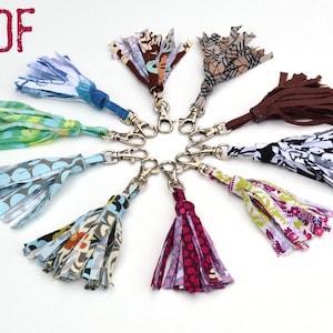 Op de afbeelding: Tien kleurrijke stoffen sleutelhangers met zilveren sleutelringen. De sleutelhangers zijn gemaakt van stofresten en hebben een kwastontwerp. De sleutelhangers zijn in een cirkel op een witte achtergrond gerangschikt.