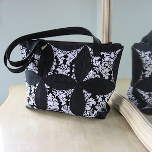 May include: A black and white quilted tote bag with a damask pattern. The bag has a zipper closure and two black straps.