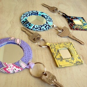 May include: Four keychains with round and square mirrors covered in fabric with different patterns. The keychains are attached to silver keys.