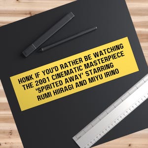 May include: Yellow bumper sticker with black text that reads "HONK IF YOU'D RATHER BE WATCHING THE 2001 CINEMATIC MASTERPIECE 'SPIRITED AWAY' STARRING RUMI HIIRAGI AND MIYU IRINO"