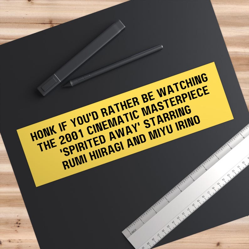 May include: Yellow bumper sticker with black text that reads "HONK IF YOU'D RATHER BE WATCHING THE 2001 CINEMATIC MASTERPIECE 'SPIRITED AWAY' STARRING RUMI HIIRAGI AND MIYU IRINO"