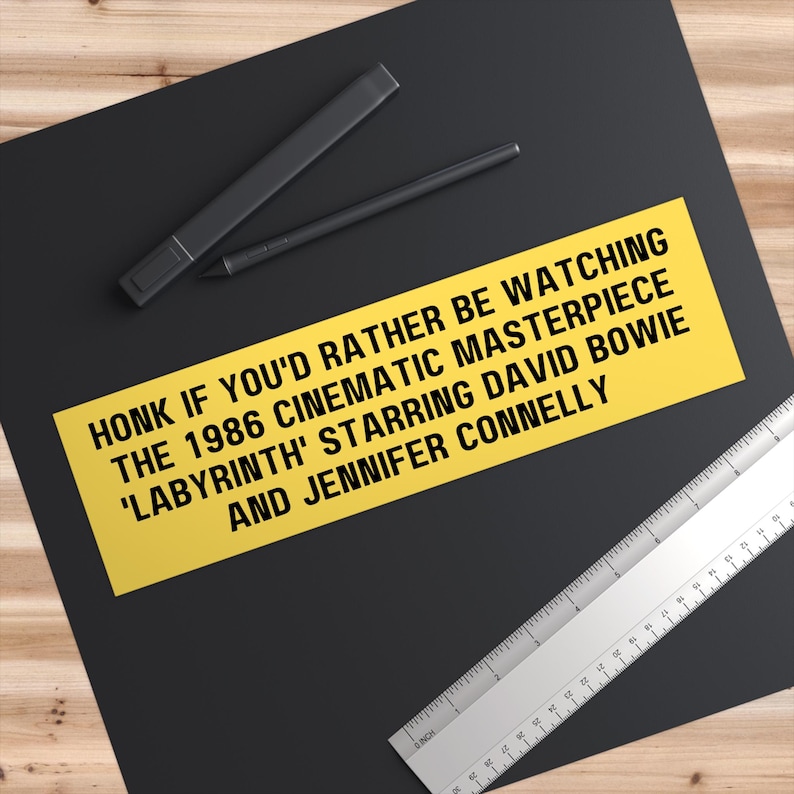 May include: Yellow bumper sticker with black text that reads "HONK IF YOU'D RATHER BE WATCHING THE 1986 CINEMATIC MASTERPIECE 'LABYRINTH' STARRING DAVID BOWIE AND JENNIFER CONNELLY"