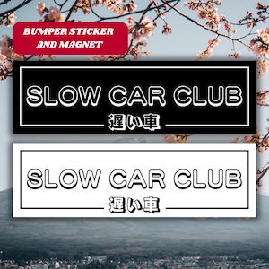 May include: Two black and white bumper stickers with the text "Slow Car Club" and the Japanese text "遅い車" which translates to "Slow Car" in English.
