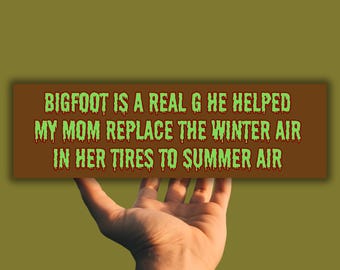 Puede incluir: Una pegatina para parachoques marrón con texto verde que dice "BIGFOOT IS A REAL G HE HELPED MY MOM REPLACE THE WINTER AIR IN HER TIRES TO SUMMER AIR".
