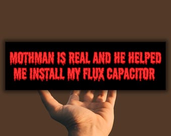 May include: A black and red bumper sticker with the text "Mothman is real and he helped me install my flux capacitor".