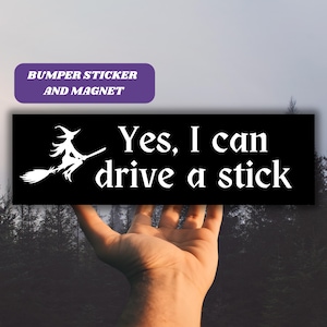 Op de afbeelding: Zwarte bumper sticker met een witte heks die op een bezem rijdt en de tekst "Ja, ik kan schakelen".