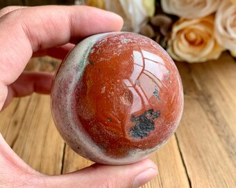 Puede incluir: Una esfera de jaspe rojo pulida con bandas blancas y negras. La esfera es lisa y tiene un acabado brillante.