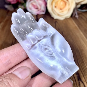 Può includere: Una scultura di mano in cristallo bianco con un palmo e dita dettagliate. La scultura è liscia e traslucida, con un leggero bagliore iridescente.