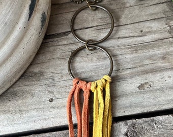 May include: A necklace featuring two brass rings and a tassel made from orange and yellow leather strands.