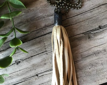May include: A white leather tassel necklace with a silver chain. The tassel is made of many thin strips of leather and hangs from a silver cap.