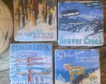 May include: Four square coasters with vintage ski resort designs. The coasters feature images of ski lifts, skiers, and ski poles. The text on the coasters reads "Beaver Creek Colorado" and "Elevation 11,490 ft".