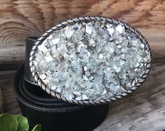May include: A black leather belt with a silver oval buckle. The buckle is covered in small, clear glass pieces.
