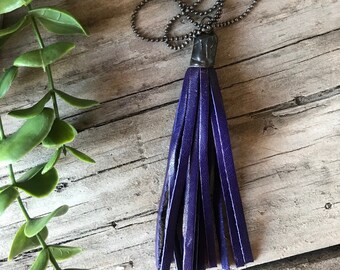May include: A purple leather tassel necklace with a silver chain. The tassel is hanging from a silver pendant.