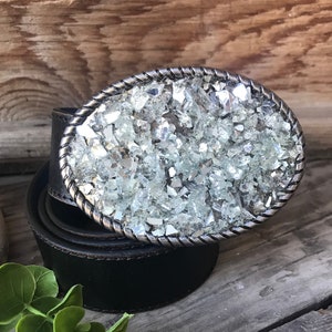 May include: A black leather belt with a silver oval buckle. The buckle is covered in small, clear glass pieces.