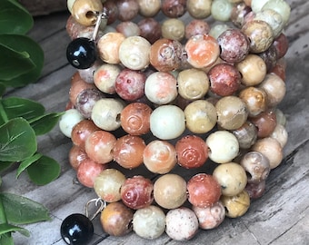 May include: A multi-strand bracelet made of round, multi-coloured, patterned beads. The beads are a mix of light brown, beige, and pink with a swirling pattern. The bracelet has two black bead accents.