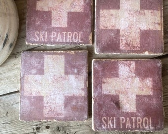 May include: Four square red coasters with a white cross and the text "SKI PATROL" in white. The coasters have a distressed, vintage look.