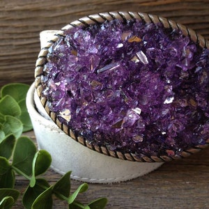 May include: A white leather belt with a silver buckle featuring a purple amethyst crystal design.
