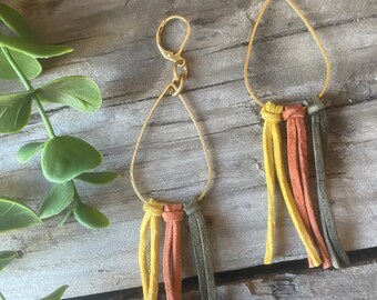 May include: A pair of gold teardrop-shaped earrings with leather tassels in yellow, orange, and dark green.