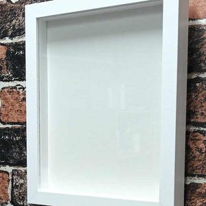 May include: A white square shadow box frame with a clear glass front. The frame is made of wood and has a simple, modern design.