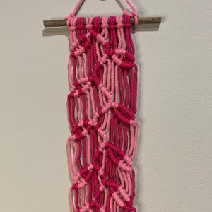 May include: A pink and hot pink macrame wall hanging with a wooden dowel at the top.