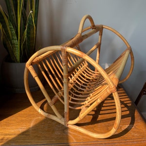 May include: A natural woven bamboo magazine rack with a curved design. The rack is made of light brown and natural colored bamboo.