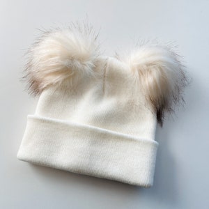 white knitted kids hat with 2 faux fur pom poms on top