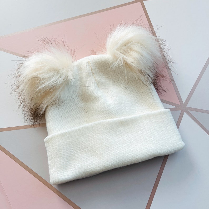 white knit infant hat with two pom poms