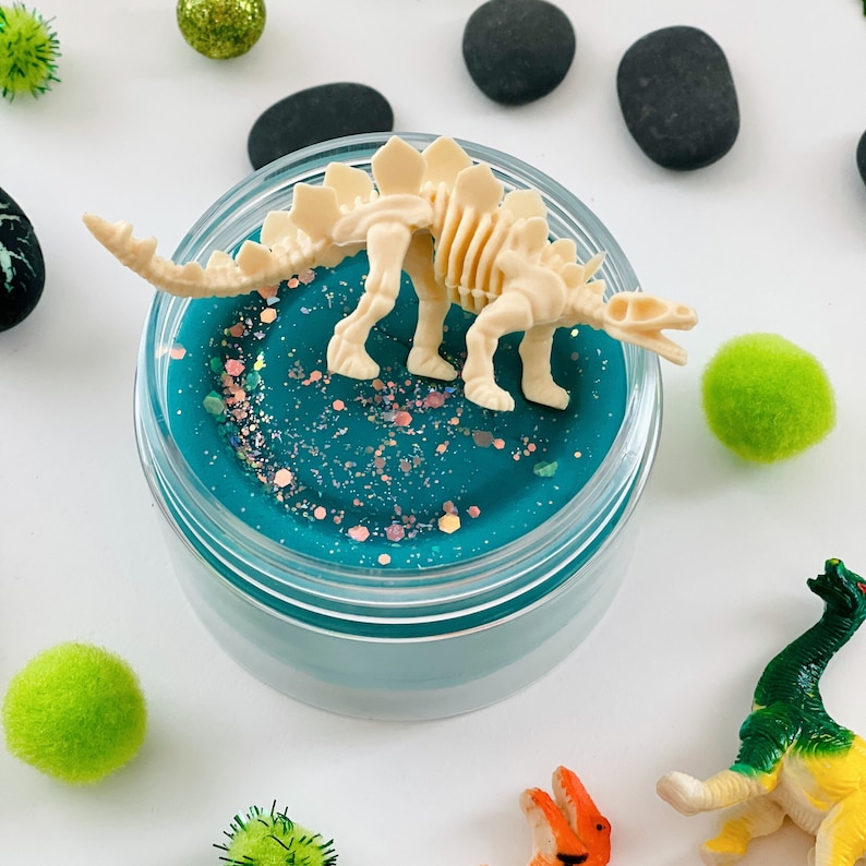 dinosaur skeleton sitting on top of a blue scented sensory playdough jar kit
