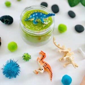 dinosaur sitting on top of a green sensory playdough kit jar