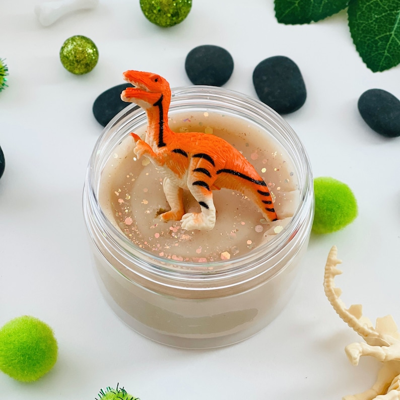 orange dinosaur sitting on top of a scented playdough sensory kit jar