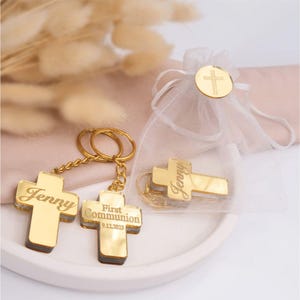May include: Gold cross keychain with the name "Jenny" and the text "First Communion 9.12.2023" engraved on it. The keychain is packaged in a white organza bag with a gold cross charm.
