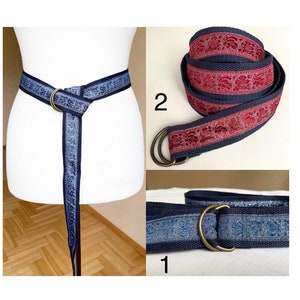 Può includere: Due stili diversi di cinture intrecciate con un motivo floreale decorativo. Una cintura è blu navy con un motivo floreale argentato e l'altra è blu navy con un motivo floreale rosso. Entrambe le cinture hanno un anello a D in ottone.