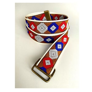 Può includere: Una cintura intrecciata con motivo bianco, marrone, rosso e blu con fibbia in ottone.